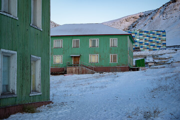 Three green buildings in front of a snow covered mountain in an old mining town called "Barentsburg" on Spitsber