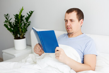 happy handsome man lying on bed and reading book
