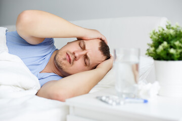 Fototapeta na wymiar health care and illness concept - sick man with fever or headache lying on bed at home or hospital