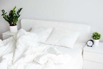 unmade bed with white blanket and two pillows at home or hotel