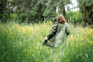 A girl walks along a flowering field. Beautiful field with yellow flowers and green grass. Goes forward.
