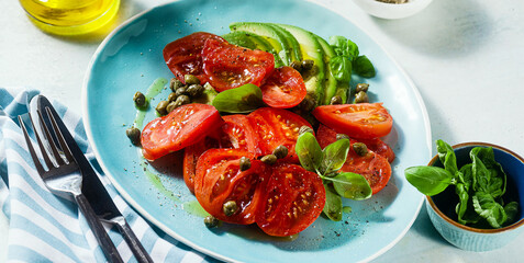 banner of summer salad with ripe tomatoes and avocado with capers in a blue plate on the table