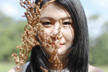 Beautiful asian woman in white dress relax and smiling with Dry wood stalks  in natural park. Young Thai girl enjoy on holiday with sunlight in garden.