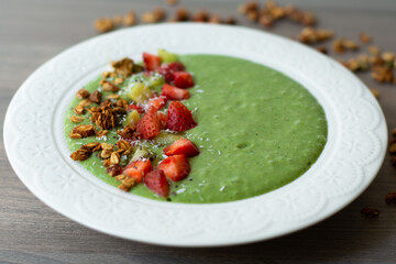 Green smoothie bowl with banana, strawberry, spinach, kale, kiwi, coconut milk garnished with homemade oat, nut and seed granola, coconut flakes, chia seeds, kiwi and strawberry