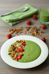 Green smoothie bowl with banana, strawberry, spinach, kale, kiwi, coconut milk garnished with homemade oat, nut and seed granola, coconut flakes, chia seeds, kiwi and strawberry