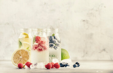 Berry and citrus fruit infused summer cold drinks in glass bottles on gray stone table background, copy space