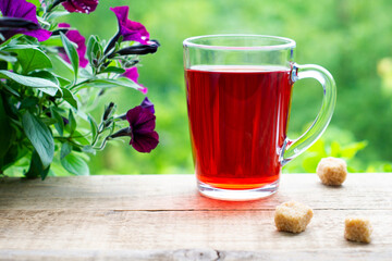 Hibiscus tea in a glass cup on a wooden table on the green background.  Slices of cane sugar near a cup. Good morning mood and a charge of positive energy