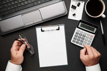 Top view of businessman's hands working. Modern black office desk with laptop, notebook, pencil and a lot of things. Flat lay table layout. Copy space for text.