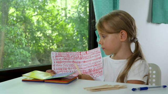 Child little girl does math school homework and counting in elementary school online at home. Distance education with children, online class
