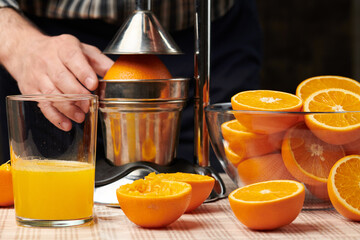 Squeezing an orange with a manual press, close view, making a glass of fresh. Fresh oranges on a wooden table, whole, squeezed and sliced.