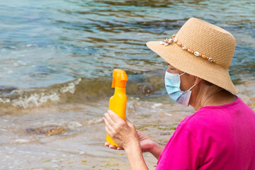 senior woman with medical mask and suntan lotion on the beach, prevention against viruses and infections in summer