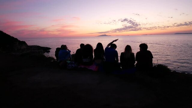 silhouette of a group of kids watching the sunset on the Sorrento coast with Ischia and Procida in background. Naples, Campania, Italy.