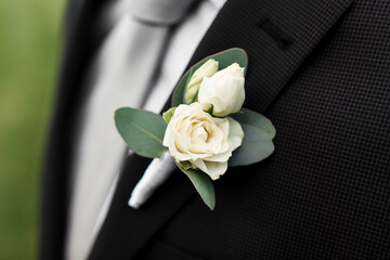 boutonniere of the groom. white rose close-up. gray tie and black jacket