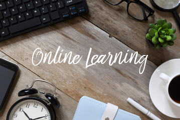 Top view of mobile phone,notebook, vintage alarm clock,pen, a cup of coffee, plant,glasses,magnifying glass and computer notebook on wooden background written with Online Learning.
