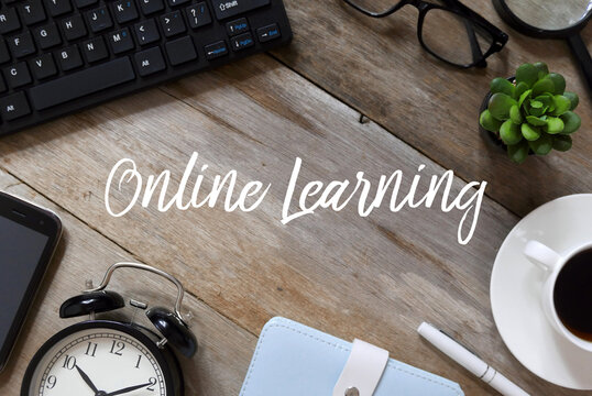 Top view of mobile phone,notebook, vintage alarm clock,pen, a cup of coffee, plant,glasses,magnifying glass and computer notebook on wooden background written with Online Learning.