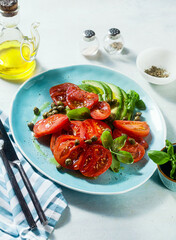 summer salad with ripe tomatoes and avocado with capers in a blue plate on the table