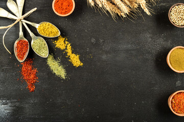 Top view of different kinds of colorful spices in spoons on black stone surface. Creative food concept texture with blank copy space for your message. - Powered by Adobe