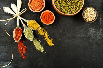 Top view of different kinds of colorful spices in spoons on black stone surface. Creative food concept texture with blank copy space for your message.