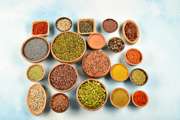 Top view of different kinds of colorful spices in wooden bowls on white surface.