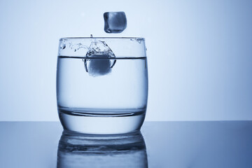 Ice falls into a glass of water with splashes, drops and air bubbles.