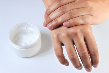 Closeup brunette woman applying cream on her hands. White cream box on isolated white background. Soft skin concept.