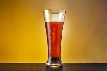 Tall glass of cold tea on warm yellow background. Fresh summer beverage.