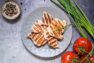 Grilled  chicken on the grey plate with pepper, garlic, green onion and tomatoes.Top view. Grey background. Healthy food.