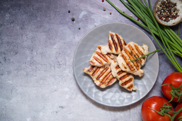 Grilled  chicken on the grey plate with pepper, garlic, green onion and tomatoes.Top view. Grey background. Healthy food. There is place for recipe.
