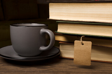 Closeup of cup of hot coffee, stack of book and empty tag near, wooden desk.Relax and reading