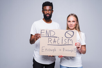 Young african man and coucasian woman holding a cardboard poster with the message text END RACISM...