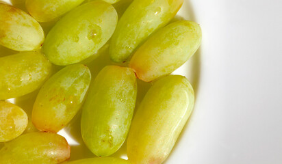 Macro detail shot of tasty green grapes on a white porcelain plate. Space for text on the right.