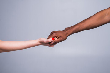 White caucasian female hand and black African American male hand holding fingers together in world unity and racial love and understanding in tolerance and races diversity. 