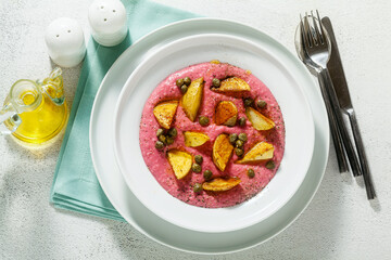 summer dish with pink hummus from cannellini beans and beets with fried potatoes and capers in a plate on the table