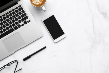 White marble office desk table with laptop computer, smartphone with blank screen, cup of latte...