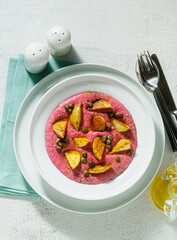 summer dish with pink hummus from cannellini beans and beets with fried potatoes and capers in a plate on the table