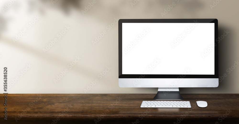 Fototapete desktop computer on wood table backgorund with sunlight window create leaf shadow on wall with blur indoor green plant foreground.panoramic banner mockup for display of product,warm tone lights