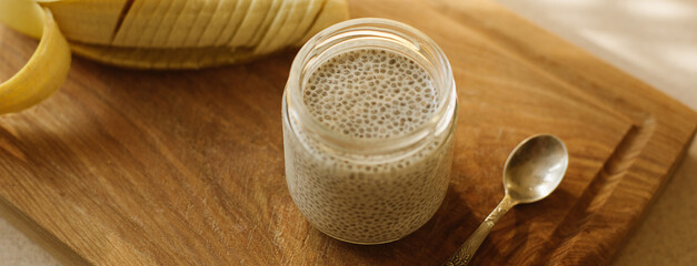 Dessert bowl of tasty chia seed pudding and banana on wooden table on white background. Banner for website