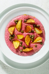 summer dish with pink hummus from cannellini beans and beets with fried potatoes and capers in a plate on the table