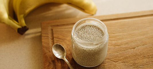Dessert bowl of tasty chia seed pudding and banana on wooden table on white background. Banner for website