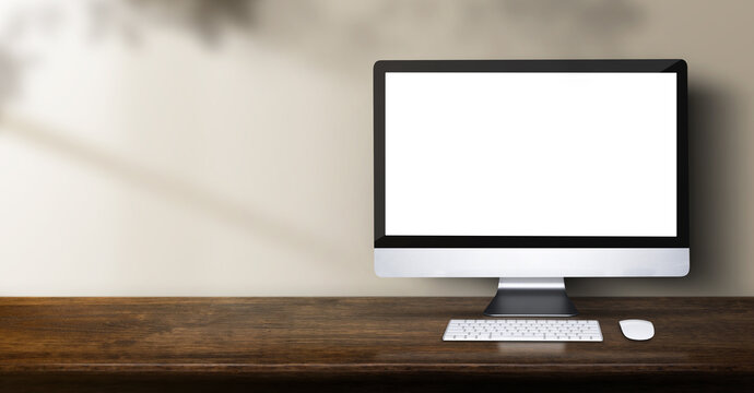 desktop computer on wood table backgorund with sunlight window create leaf shadow on wall with blur indoor green plant foreground.panoramic banner mockup for display of product,warm tone lights