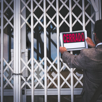 Lockdown And Bankrupt Economy Crisis Concept With Unrecognizable Store Owner Putting Closed Sign On The Door - People And Business End Coronavirus Covid-19 Pandemic Emergency - Cerrado Is Spanish