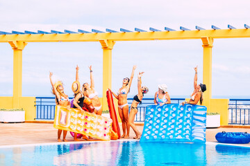 Group of happy women enjoy together the blue water swimming pool with coloured bikini and lilos and...