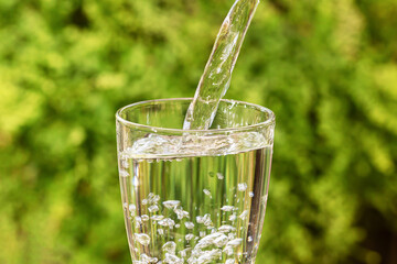 Pouring drinking water into glass on blurred green nature background