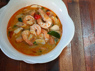 Tom Yum goong or hot and sour soup with prawns, served in a ceramic bowl  on wood table. Tom Yum is the welkown and popular Thai spicy soup.