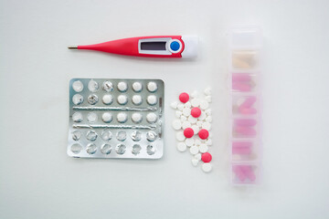 Pink thermometer with pills and tablets on white background