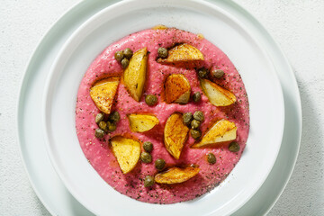summer dish with pink hummus from cannellini beans and beets with fried potatoes and capers in a plate on the table