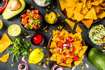 Nachos chips with melted cheese and various traditional mexican dips, salsa and jalapeno, dark grey background top view copy space