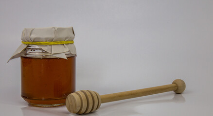 Glass jar with honey and a wooden stick on a white background
