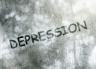 Depression word drawing on fogged window glass. Depression mood concept. Grey colors.