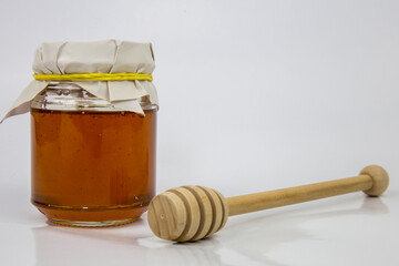 Glass jar with honey and a wooden stick on a white background